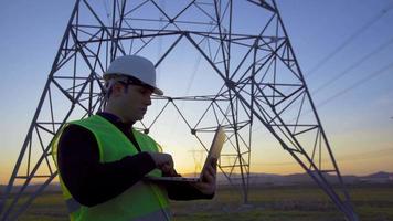 ingegnere che esamina i poli elettrici. ingegnere che lavora al computer portatile al tramonto e guarda i poli elettrici. video