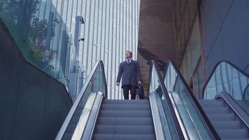 hombre de negocios bajando la escalera mecánica. joven empresario moderno en traje con maletín. video