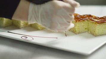 The chef decorates the dessert plate. Chef drawing ornament with chocolate sauce on the edge of dessert plate. video