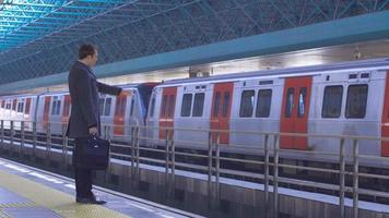 zakenman wachten op metro. zakenman die op de metro wacht en op zijn horloge kijkt. moderne zakenman met aktentas in de hand. video