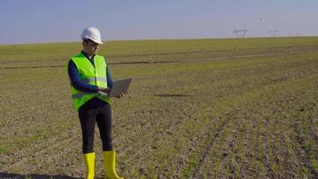 ingenjör som arbetar på jordbruksmark. ingenjör stående på jord som arbetar med bärbar dator. han gör analys. han gör anteckningar på den bärbara datorn. modernt och tekniskt jordbruk. video
