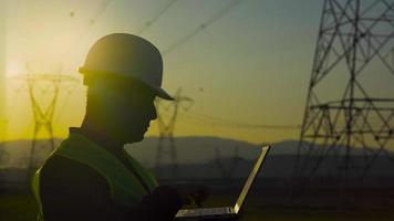 ingeniero trabajando frente a postes eléctricos. ingeniero trabajando frente a torres eléctricas, silueta de ingeniero al atardecer. ingeniero eléctrico. video