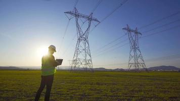 ingeniero eléctrico trabajando frente a líneas de alta tensión. un ingeniero que trabaja en una tableta en el área de líneas de alta tensión. ingeniero eléctrico haciendo inspección de campo. video