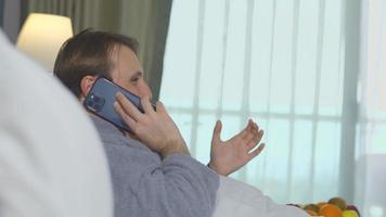 hombre acostado en la cama hablando por teléfono. hombre acostado en la cama haciendo una llamada telefónica. entrevista de trabajo. video
