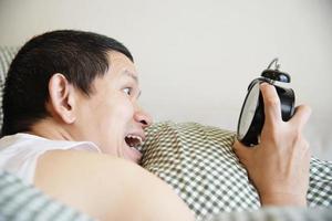 Sleepy man holding the alarm clock in the morning with late wake up - every day life at home concept photo