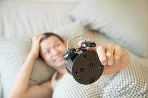 hombre soñoliento sosteniendo el despertador por la mañana con despertar tardío - concepto de vida diaria en casa foto