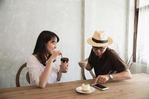 hombre y mujer casuales hablando alegremente mientras toman café y miran el teléfono móvil - estilo de vida feliz en la cafetería foto