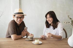 hombre y mujer casuales hablando alegremente mientras toman café y miran el teléfono móvil - estilo de vida feliz en la cafetería foto