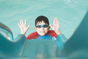 Asian happy kid playing slider in swimming pool photo