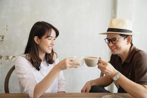 hombre y mujer casuales hablando alegremente mientras toman café y miran el teléfono móvil - estilo de vida feliz en la cafetería foto