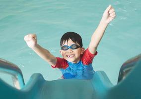 Asian happy kid playing slider in swimming pool photo