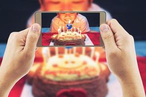 Close up of people take photo of a boy ready to blow birthday cake party using mobile phone - happy birthday celebration concept
