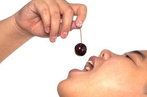 Asian boy is holding ripe cherry ready to put into his open mouth over white background photo