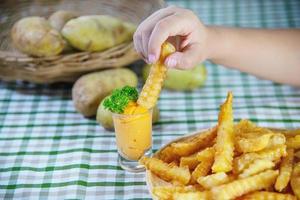 Hand holding delicious fried potato on wooden plate with dipped sauce - traditional fast food concept photo