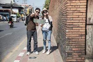 Asian backpack couple tourist holding city map crossing the road - travel people vacation lifestyle concept photo