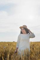 mujer adulta media con vestido blanco parada en un campo de trigo con amanecer en el fondo, vista trasera foto