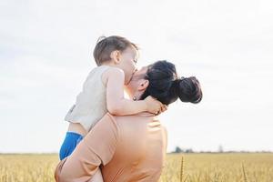 Happy family of mother and infant child walking on wheat field, hugging and kissing photo