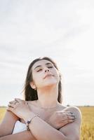 mujer joven en vestido blanco de pie en un campo de trigo con el amanecer en el fondo foto