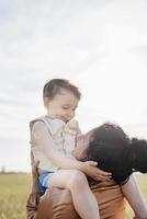 Happy family of mother and infant child walking on wheat field, hugging and kissing photo