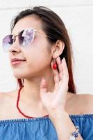 mujer joven elegante con camisa de jeans, gafas de sol y joyas rojas en la calle, fondo de pared blanca foto