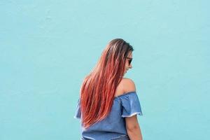 alegre mujer de moda con el pelo rojo bailando sobre fondo de pared azul en la calle foto