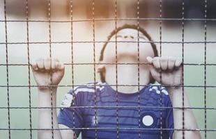 Dark portrait of a boy stand behind and holding steel screen or chain link fence - stressed sad child with no freedom concept photo