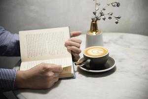 el hombre lee un libro con una hermosa taza de café fresco y relajante por la mañana - la gente se relaja y el concepto de fondo del estilo de vida del café foto