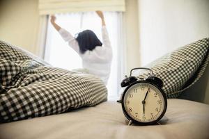 Sleepy woman reaching  holding the alarm clock in the morning with late wake up - every day life at home concept photo