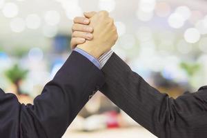 Close up of two business man holding hands firmly over modern office with bokeh background photo