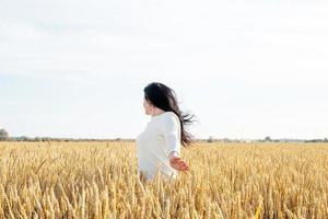 mujer adulta media con vestido blanco parada en un campo de trigo con amanecer en el fondo, vista trasera foto