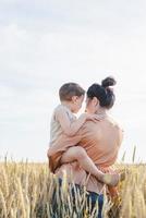 Happy family of mother and infant child walking on wheat field, hugging and kissing photo