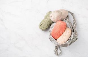 pastel colored yarn wool in a fabric shopping bag on marble background photo