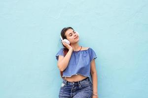 alegre mujer de moda con el pelo rojo escuchando la música en el fondo de la pared azul en la calle foto