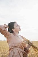 mujer adulta media con camisa beige parada en un campo de trigo con amanecer en el fondo, vista trasera foto