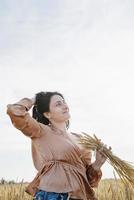 Mid adult woman in beige shirt standing on a wheat field with sunrise on the background, back view photo