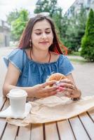 Elegante mujer milenaria comiendo hamburguesas en un café de la calle en verano foto