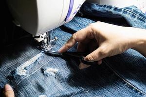 Woman doing jeans patchwork using sewing machine - home DIY sewing concept photo