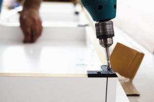 el hombre está trabajando con el montaje de muebles usando un destornillador eléctrico en la instalación de una nueva casa - trabajo técnico en el lugar usando el concepto de herramientas manuales foto