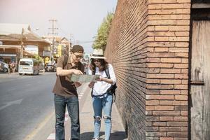 mochila asiática pareja turista sosteniendo un mapa de la ciudad cruzando la carretera - gente de viaje concepto de estilo de vida de vacaciones foto