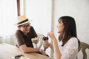 hombre y mujer casuales hablando alegremente mientras toman café y miran el teléfono móvil - estilo de vida feliz en la cafetería foto