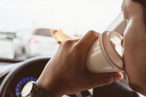 Business man eating pizza and coffee while driving a car dangerously photo