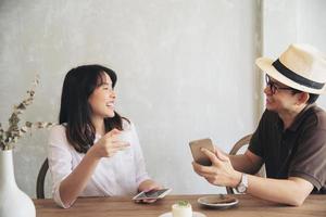 hombre y mujer casuales hablando alegremente mientras toman café y miran el teléfono móvil - estilo de vida feliz en la cafetería foto