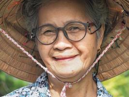 anciana asiática con sombrero sonriendo mientras está de pie en un jardín foto