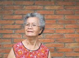 una anciana asiática de pie y mirando a la cámara con fondo de pared de ladrillo foto