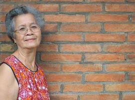 una anciana asiática de pie y mirando a la cámara con fondo de pared de ladrillo foto