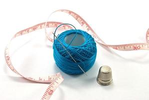 Thimble,needles and blue thread ball  for sewing on a background thread photo