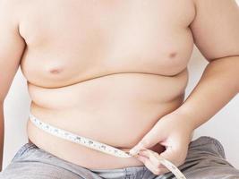 A fat boy is measuring his belly using tape meter photo