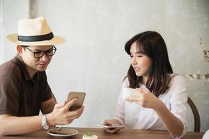 hombre y mujer casuales hablando alegremente mientras toman café y miran el teléfono móvil - estilo de vida feliz en la cafetería foto