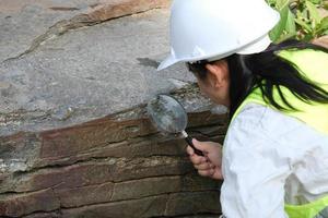 investigadora geóloga asiática analizando rocas con una lupa en un parque natural. geólogo de exploración en el campo. concepto de piedra y ecología. foto