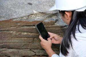 una investigadora geóloga asiática está analizando rocas con un teléfono inteligente en un parque natural. geólogo de exploración en el campo. concepto de piedra y ecología. foto